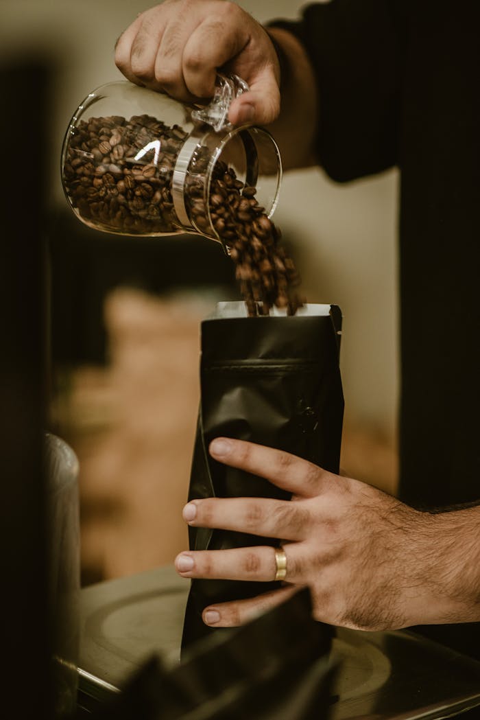 Close-up of hands pouring coffee beans into a bag, capturing fresh aroma and rich texture.