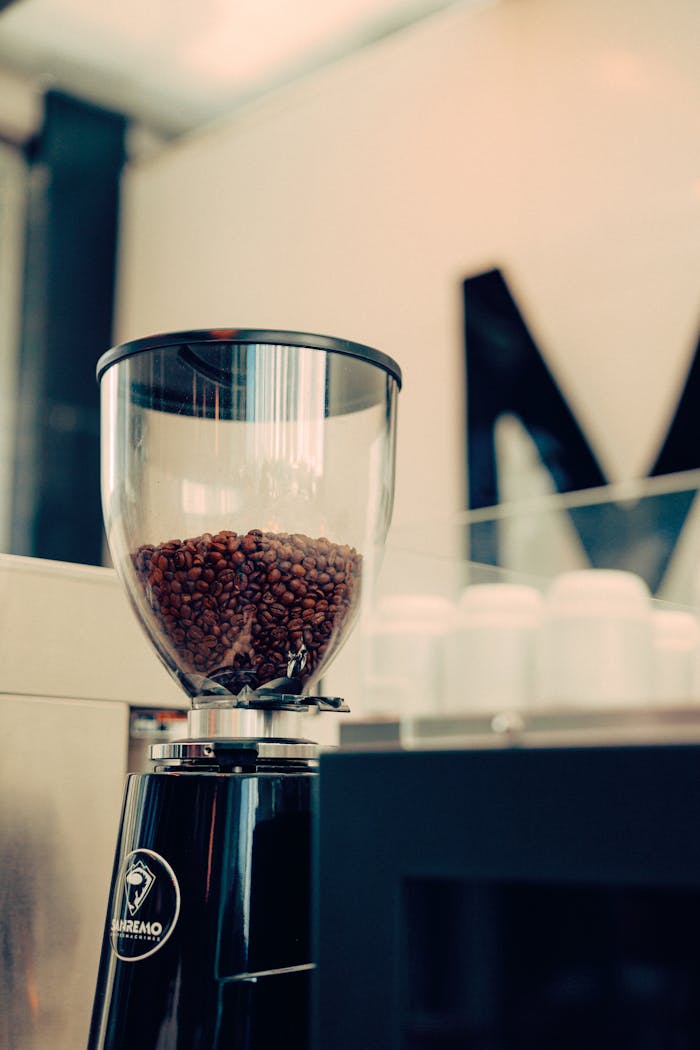 Close-up of a modern coffee grinder filled with beans, set in an artisan cafe environment.